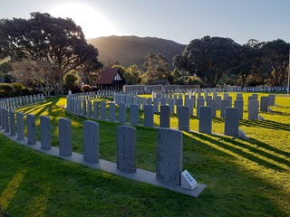 Anzac headstones in semi-circle lines at Karori Cemetery with sun shining over the hill.