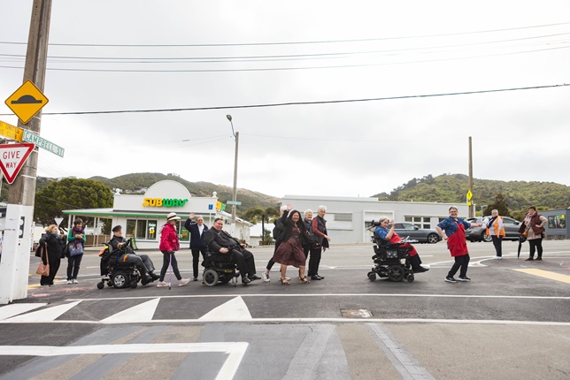 A group of senior citizens including three in wheelchairs, re-enact the Beatle's Abbey Road album cover as they cross the road over a pedestrian crossing.
