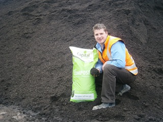 A man holding a compost bag in front of a big pile of compost.